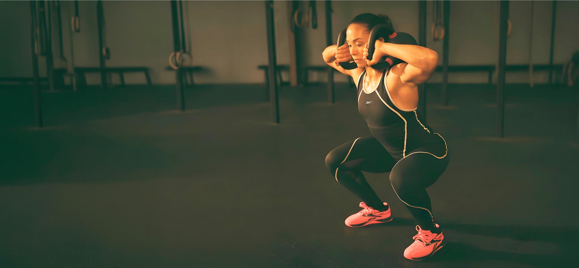 Imagen de mujer haciendo sentadillas con pesas usando tenis naranjas, REEBOK