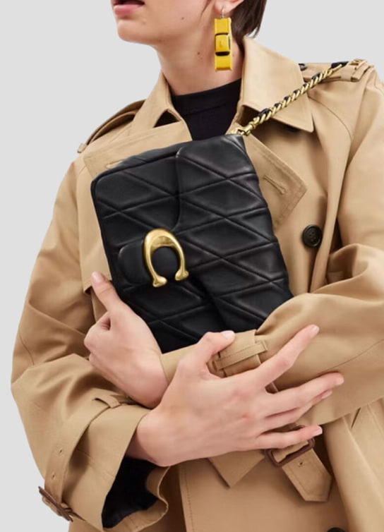 Mujer con gabardina cafe, lleva un bolso color negro COACH