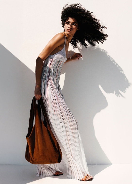 Mujer usando vestido largo color blanco y lleva un bolso grande color cafe