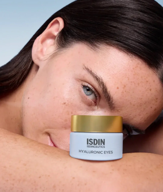 Mujer recargando su rostro sobre su brazo junto a un frasco de crema para ojos ISDIN