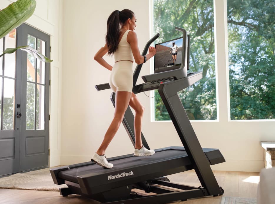 Mujer con ropa deportiva haciendo ejercicio en su casa con una caminadora 