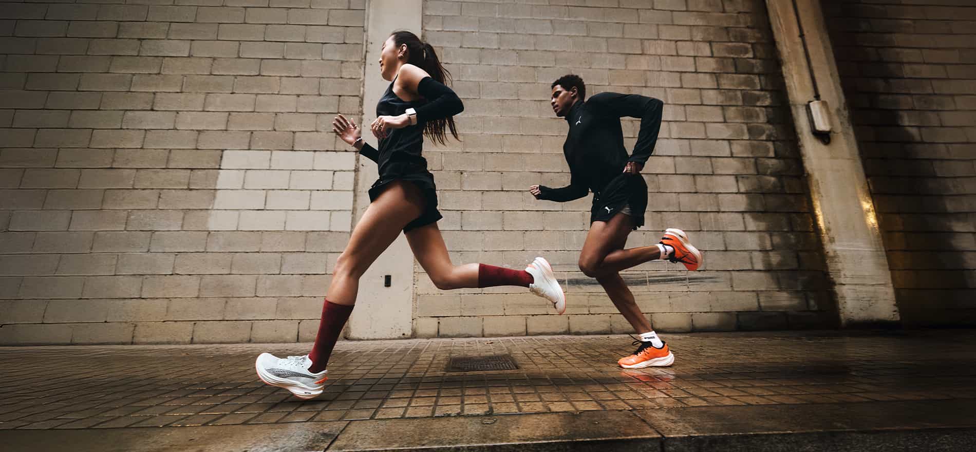 Imagen de dos personas corriendo con playera, short negros y tenis PUMA