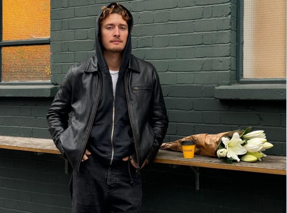 Hombre en la calle, lleva sudadera negra, chamarra de pier color negra y pantalon negro STREETWEAR