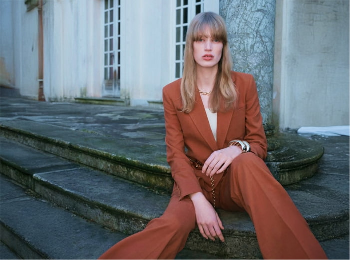 Mujer sentada en una banqueta, con traje color marron 