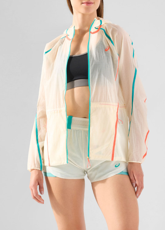 Mujer con top color negro, short blanco y sudadera transparente con rayas verdes y rojas, ASICS