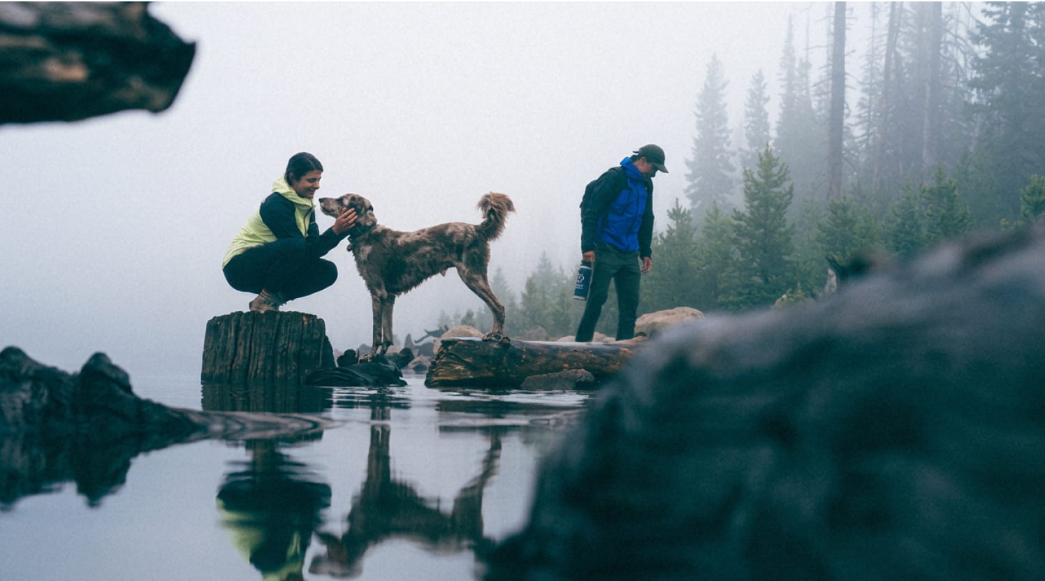 Personas con chamarras impermeables The North Face junto a su perro en un lago boscoso con neblina