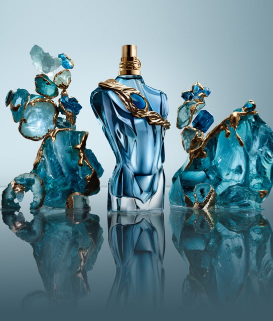 Botella de perfume azul con detalles dorados rodeada de cristales turquesa