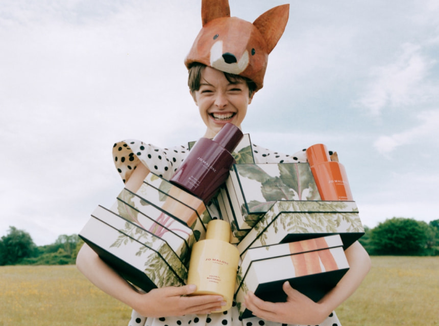 Mujer sonriendo con sombrero de zorro cargando cajas de regalo y productos Jo Malone London