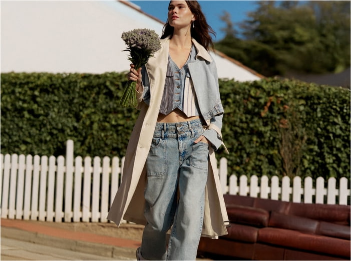 Mujer en la calle, lleva blusa blanca con azul, pantalon azul y gabardina beige