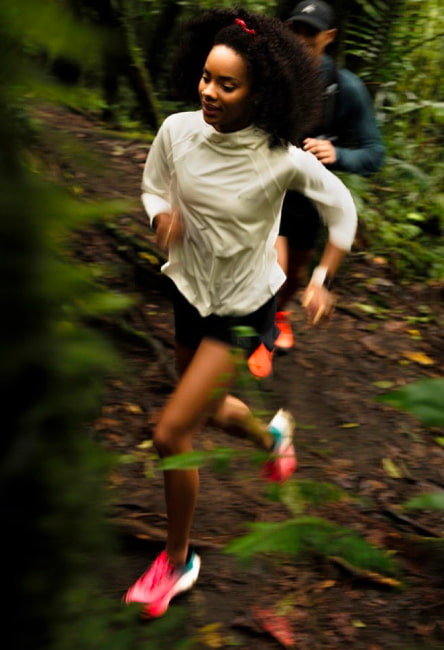 Joven corriendo en el bosque con chamarra rompevientos blanca marca Columbia