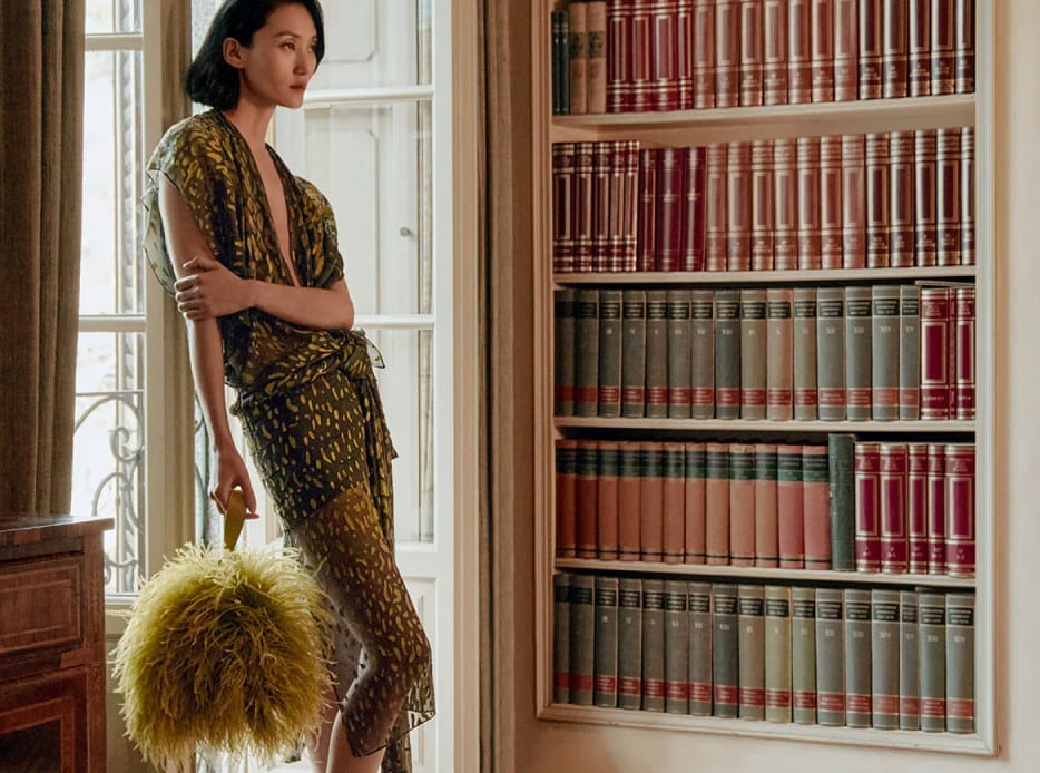 Mujer en un cuarto con libros, lleva un vestido transparente de color verde con manchas amarillas, FERRAGAMO