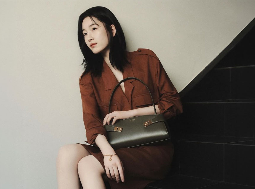 Mujer sentada con vestido caf&eacute; sosteniendo un bolso de mano Ferragamo