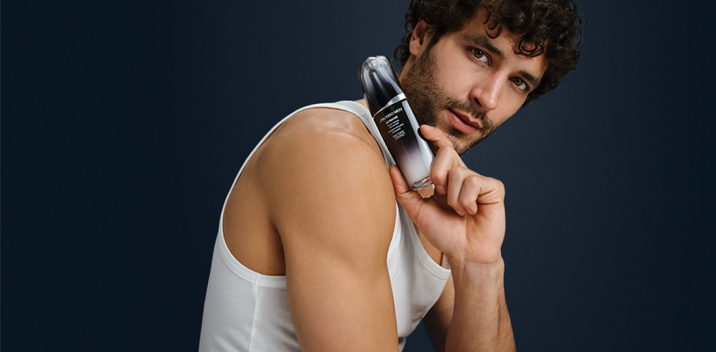 Hombre con playera de tirantes color blanca, en su mano muestra un producto para el rostro