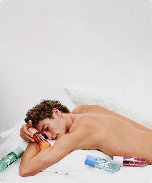 Hombre acostado en una cama, junto a el 4 envaces de perfume  de perfume CALVIN KLEIN menu