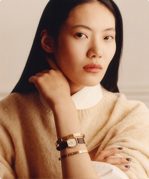 Imagen de una mujer usando un reloj dorado con extensible cafe de la marca TORY BURCH, banner menu