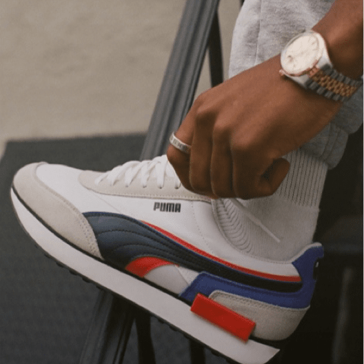 Imagen de un par de tenis de la marca PUMA color blancos con lineas rojas, negras y azul marino. Lista de marcas de hombre
