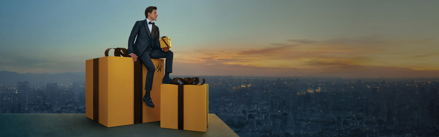 Imagen de un hombre sentado en unas cajas de regalos gigantes color marillo palacio, Navida Palacio, hasta 12 mensualidades sin intereses noviembre 21 a diciembre 24