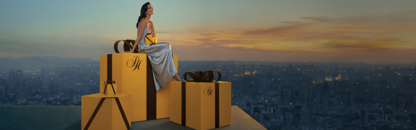 Imagen de una mujer sentada en unas cajas re regalos gigantes color marillo palacio, Navida Palacio, hasta 12 mensualidades sin intereses noviembre 21 a diciembre 24