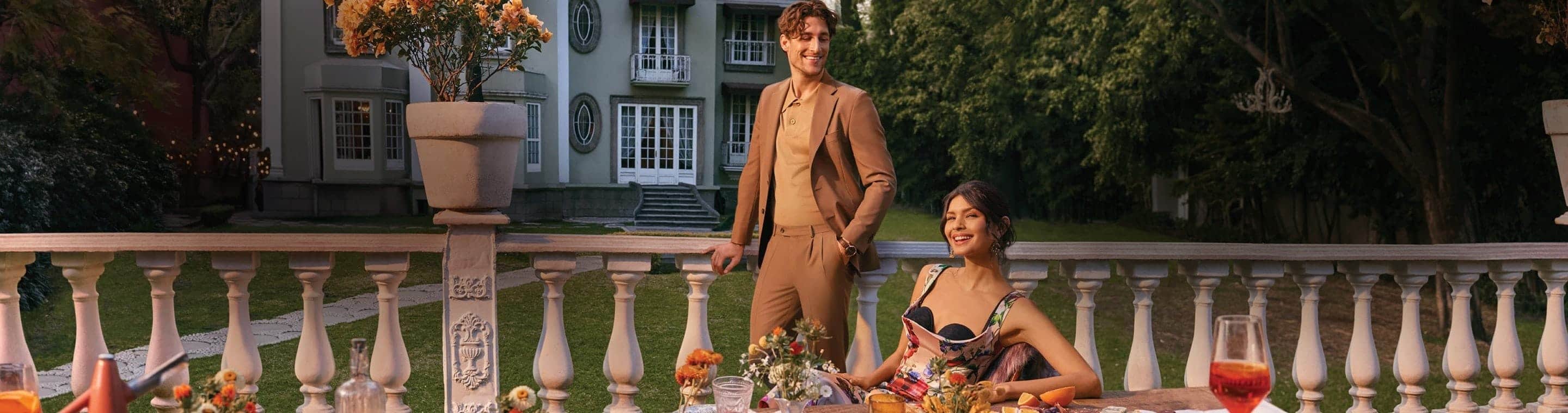 Noches Palacio Dolce Vita, Imagen de una mujer sentada con vestido estampado de flore y un hombre con traje cafe, en el jardin de una casa blanca, Hasta 20% de descuento + 12 mensualidades sin intereses + empieza a pagar en agosto*,  de abril 17 a mayo 12 del 2025