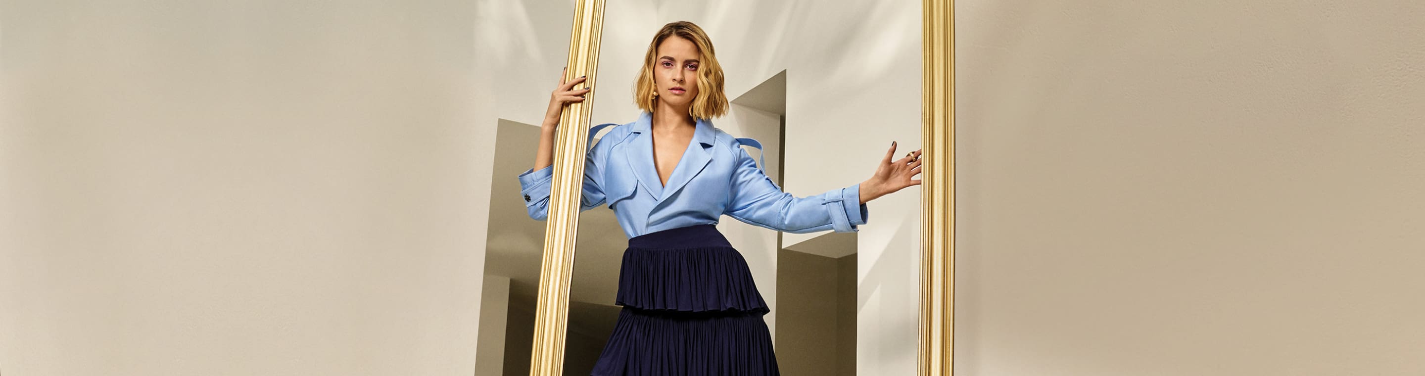 Oportunidades uanicas mujer con bluasa manga larga azul claro y falda azul marino sosteniendo un marco dorado. Hasta 40% de descuanto + hasta 3 mensualidades sin intereses, junio 16 a julio 17