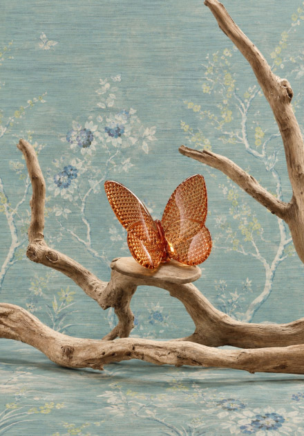 adorno de una rama seca con una mariposa de cristal color rojisa sobre ella 