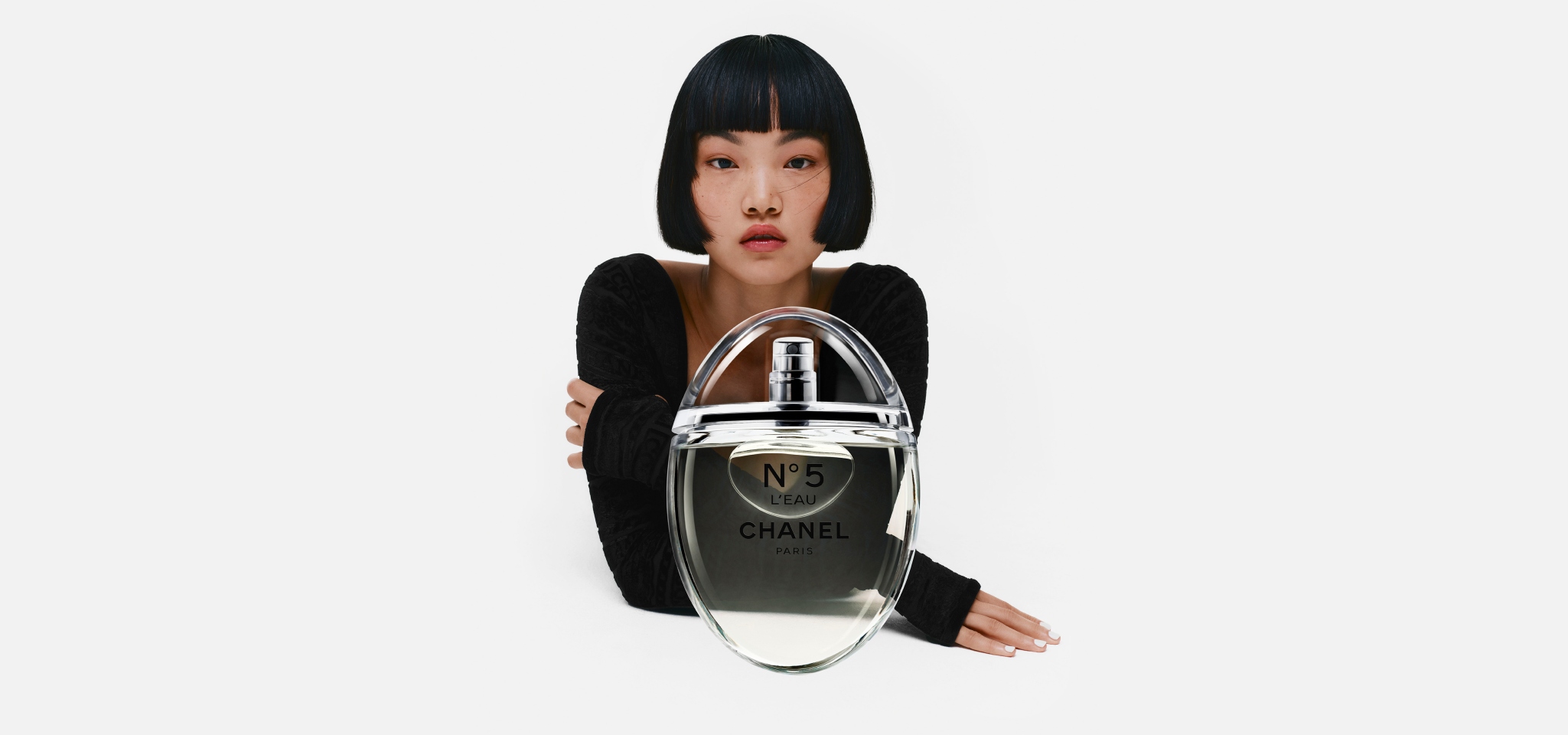 Mujer viendo al espectador, lleva blusa color negra, delante de ella un frasco de perfume Nº5 L'EAU CHANEL