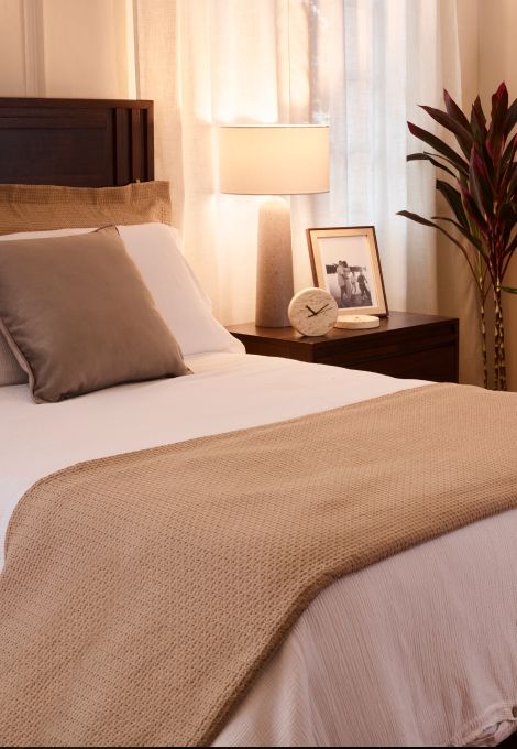 Imagen de la esquina de una habitacion donde hay una lampara alta, una mesa de madera copn marcos de fotografias