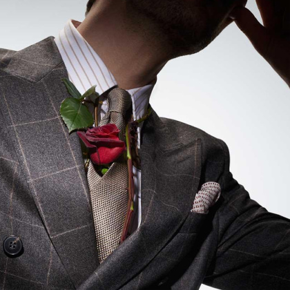 hombre con taje color gris y corbata cafe, en la corbata lleba una rosa roja