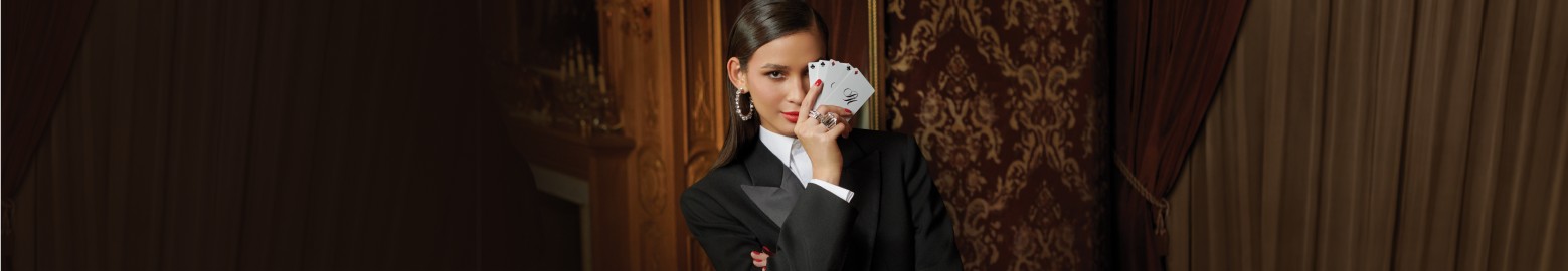 Mujer usando camisa blanca y traje negro, en su mano sostine una baraja frente a la mitad de su rostro, NOCHES PALACIO CASINO