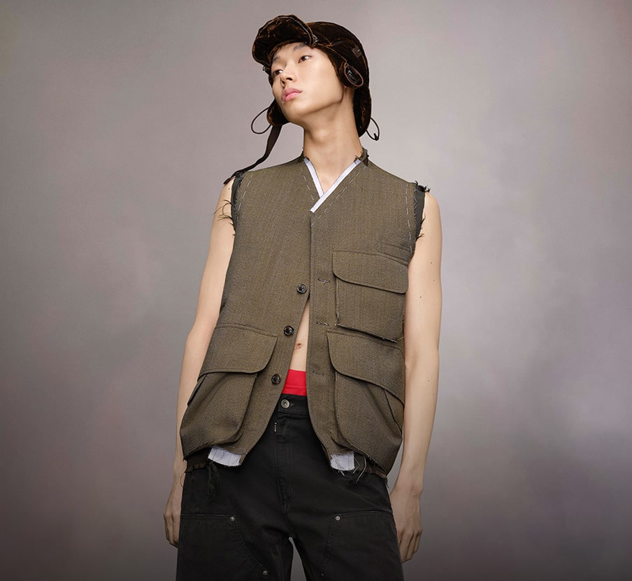 imagen de una mujer usando gorro color negro, chaleco color verde y pantalon de mezclilla color azul marino de la marca MAISON MARGIELA