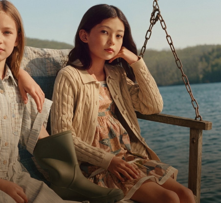 imagen de niña con ropa cafe en un columpio de madera junto a un lago con ropa de la marca POLO RALPH LAUREN