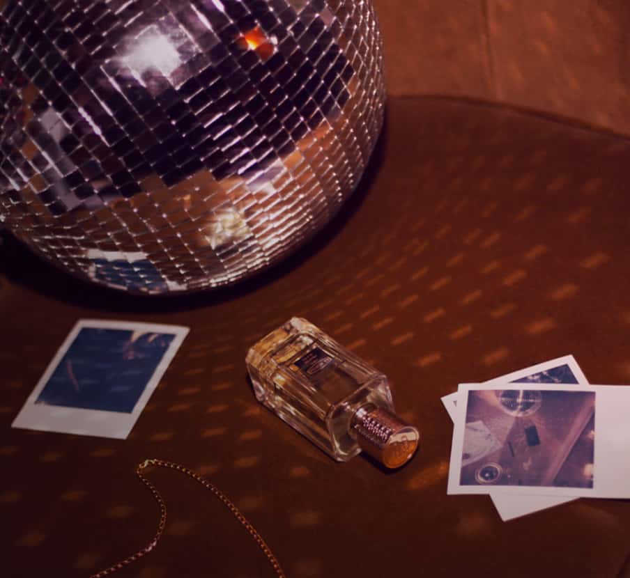 imagen botella de perfume con tapa dorada de la amrca EX NIHILO junto a bola de espejo disco