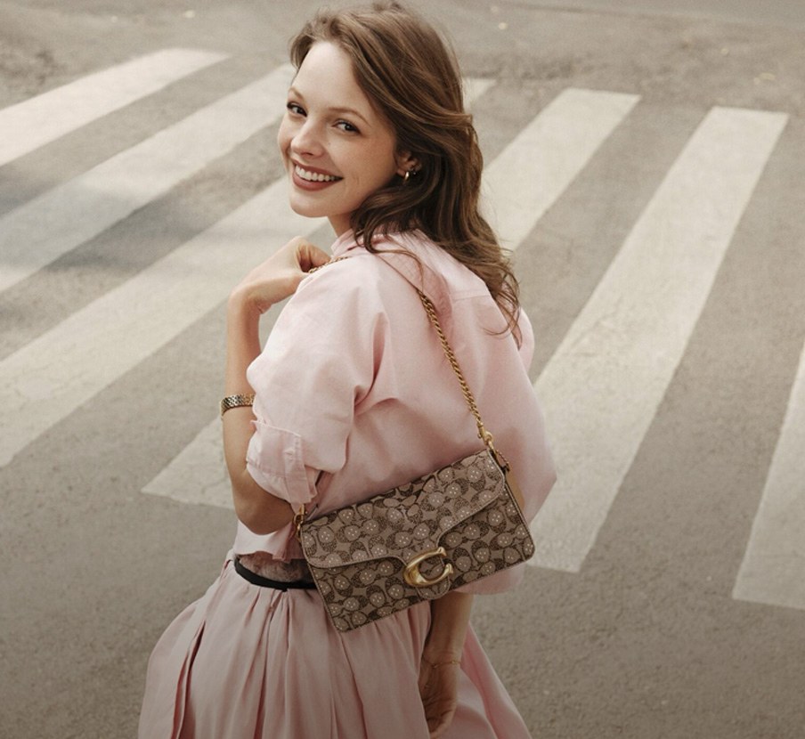 imagen de mujer con vestido rosa y bolso gris de la marca COACH