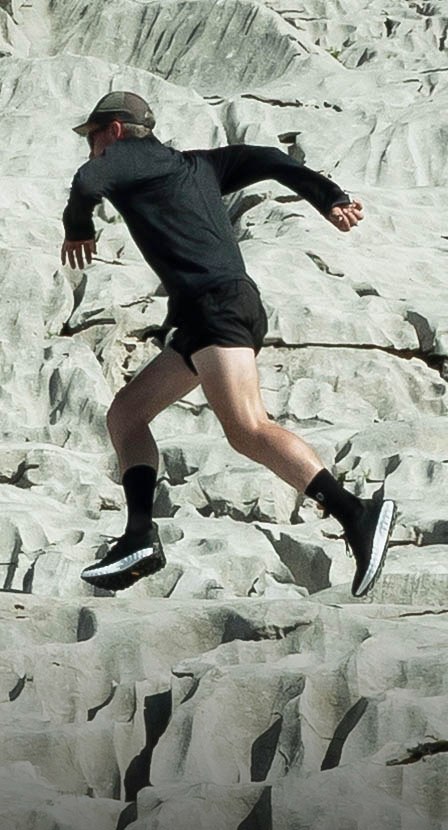 imagen de hombre corriendo con ropa negra y tenis negros con balnco de la marca NORDA