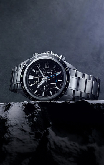 imagen de un reloj plateado con caratula negra, detalles plateados, sobre una roca 