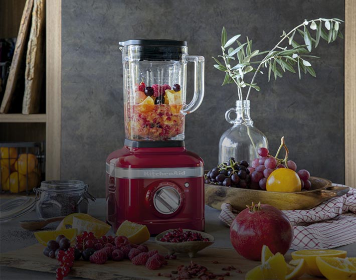 imagen de una licuadora roja en una cocina junto a frutas. KITCHEN AID