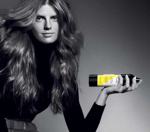 imagen mujer vestida de negro con un spray en la mano que tiene etiqueta  amarilla SISLEY