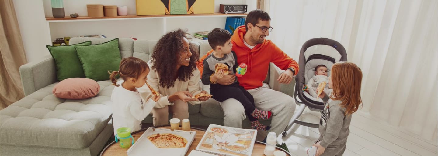 Familia sentada en una sala comiendo pizza y soneiendo, CHICCO
