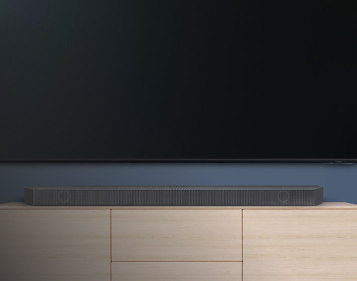 Imagen barra de audio sobre un muble de madera en un fondo azul, de la marca samsung
