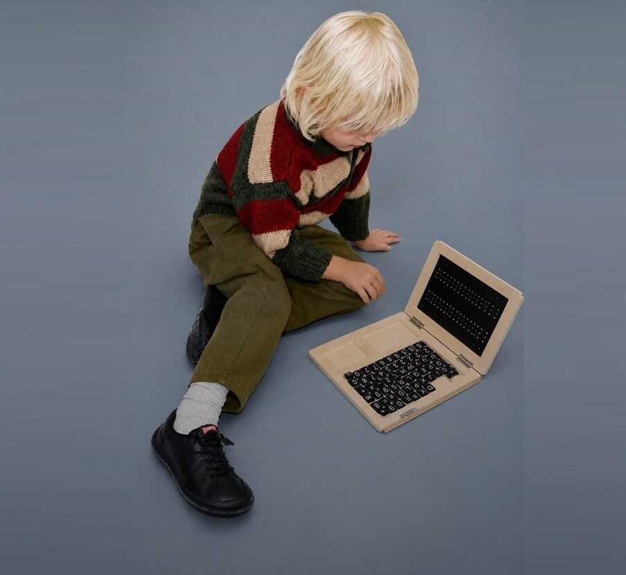 Imagen de niño con laptop dorada y zapatos negros de la marca Camper