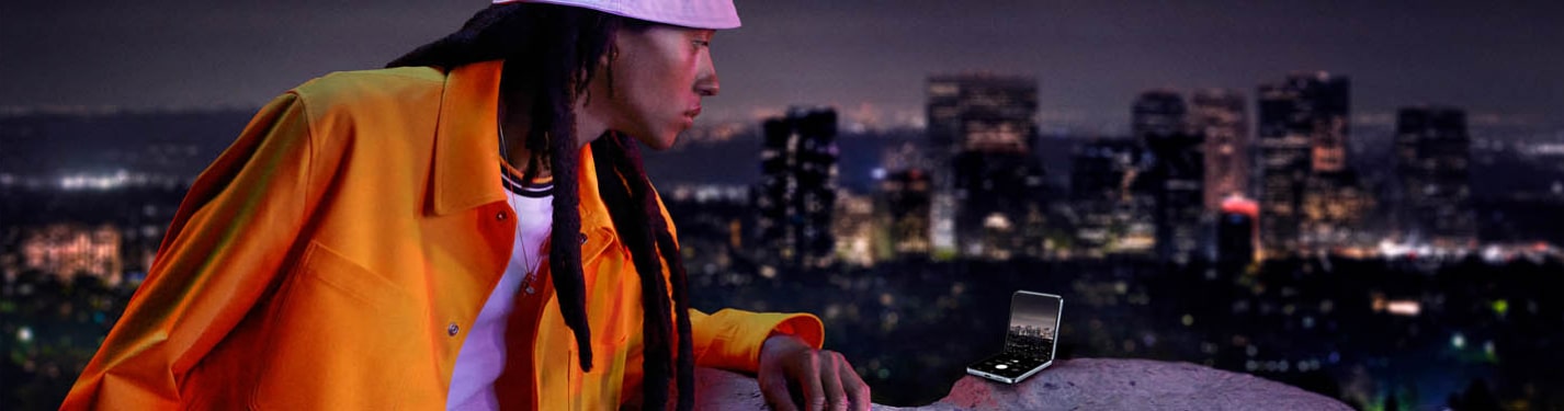 imagen de una persona con gorro blanco y chamarra naranja viendo con su celular desde una azotea con la camara de su celular de la marca samsung