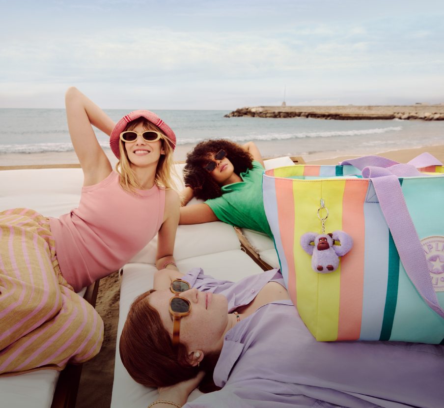 imagen de mujeres en una playa con ropa y bolsos de la marca KIPLING