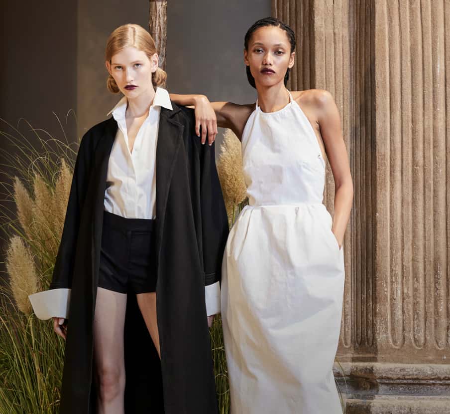 Imagen de dos mujeres, una con blusa blanca, short negro y abrigo negro y otra con vestido blanco. MAX MARA
