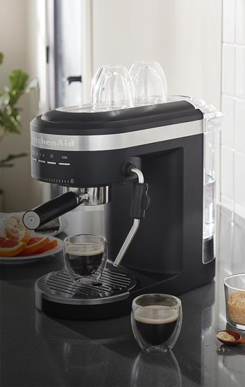 Imagen de una cocina en la cual se encuentra una cafetera de la marca KITCHEN AID, color negra de expresso con dos tazas con cafe. KITCHEN AID