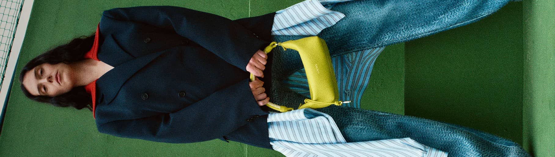 Imagen de mujer con saco azul, pantalon de mezclilla y en las manos lleva un bolso color amarillo de la marca LOEWE
