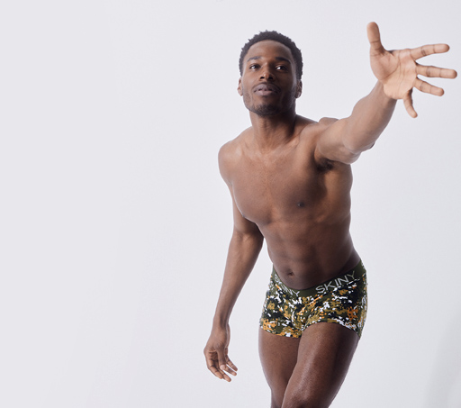 Hombre estirando el brazo, como queriendo agarras algo, lleva boxer de licra de colores. SKINY