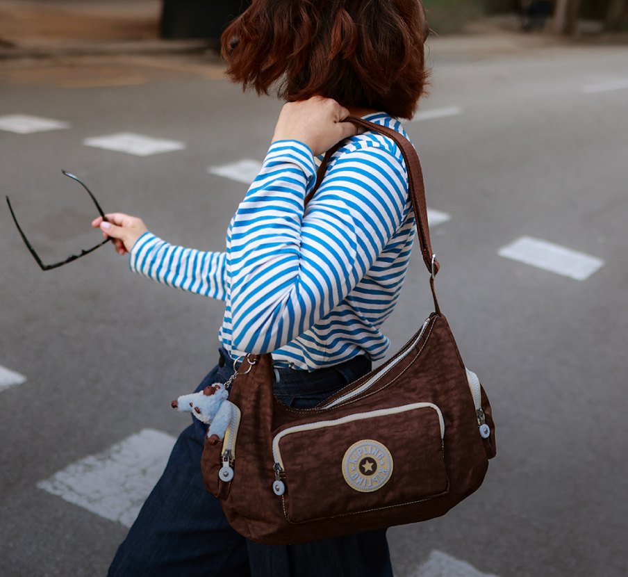 imagen de mujer con blusa a rayas azul y blanco y bolso cafe de la marca KIPLING 