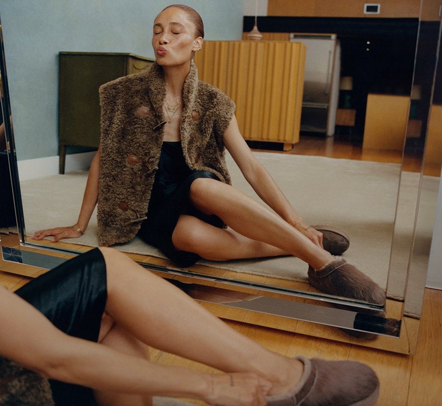 imagen de mujer con pantunflas cafes y vestido negro de la marca UGG 