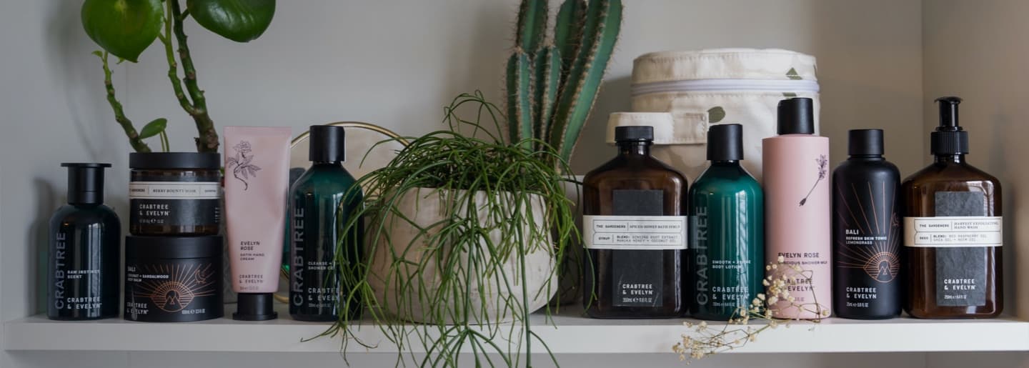 Imagen de una repisa con una serie de productos de belleza de la marca CRABTREE & EVELYN, mezclados con plantas. CRABTREE & EVELYN
