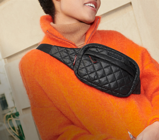 imagen de una mujer con un sueter naranja, lleva una crossbody negra de la marca MZ WALLACE